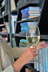 A woman selecting a book from a shelf while holding a glass of white wine, ideal for lifestyle and leisure promotions with copy space.