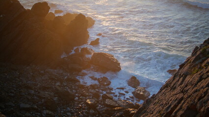 Waves splashing cliff edge in golden light. Coastal rocks sea on serene sunset