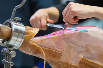 professional iberian ham cutter man cutting iberian ham and using tongs to pick it up.