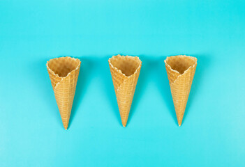 Top view of three ice cream waffle cones on blue background. Summer wallpaper, flat lay, copy space.