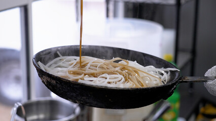 Person cooking and preparing traditional Thai cuisine in pans.