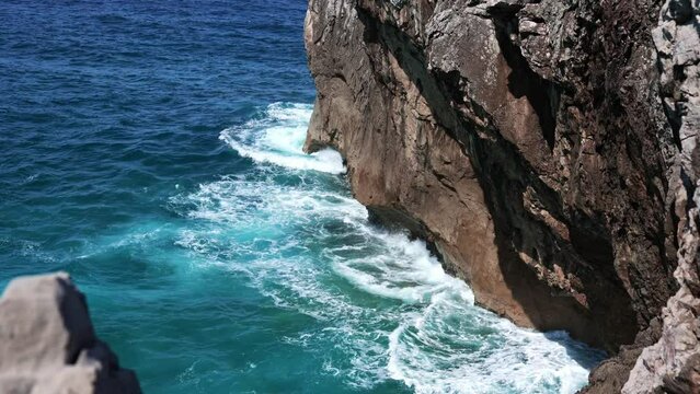 High angle shot of a rocky cliff, with waves crashing in slow motion. Travel, nature and wallpaper concept.