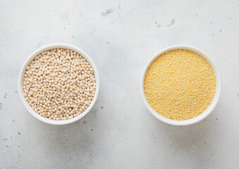 Bowls plates with dry raw white and mixed couscous seeds on light table.Macro.