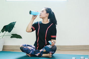 Woman take a rest and drinking water while sitting on exercise mat at home