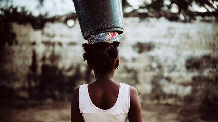 Young black African girl with a bucket on her head.