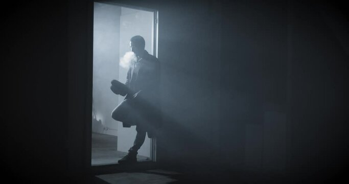 Noir film detective standing in the dark and smoking a cigarette, he is wearing a trench coat. High quality 4k footage