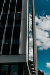 Glass facade of a modern tall office business building with clouds reflecting. White fluffy clouds Blue sky. Low angle view of skyscraper. Copy space.