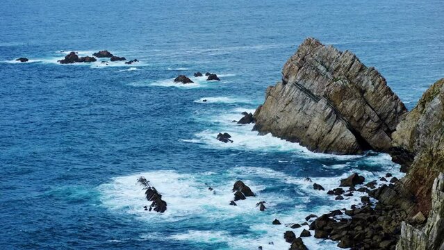 High angle shot of a rocky cliff, with waves crashing in slow motion. Travel, nature and wallpaper concept.
