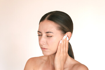 Caucasian brunette woman is experiencing acute pain in her ear. She frowns, closes her eyes,...