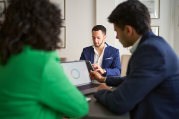 Three people are sitting at a table with laptops and a tablet