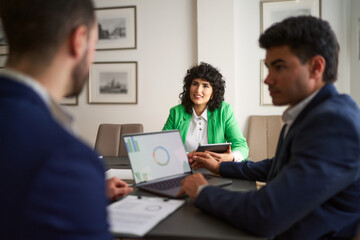 Fototapeta premium Three people are sitting at a table with laptops and papers