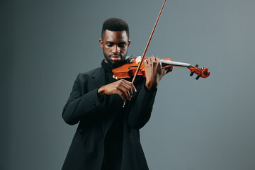 Elegant African American musician playing the violin in a black suit on a neutral gray background