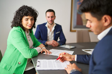 A woman in a green jacket is sitting at a table with two men in suits