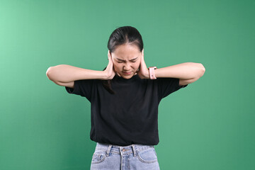 Annoyed young woman covering ears with hands isolated on green background.