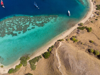 Aerial view of a curved beach with clear turquoise waters and boats anchored nearby