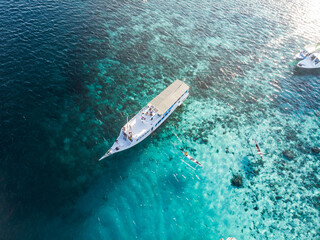 Aerial view of a catamaran over a coral reef with people swimming nearby