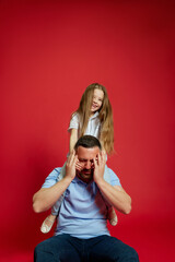 Father-Daughter Fun Time. Father enjoying playful moments with his daughter sitting on his shoulders against vibrant red background. Concept of Father's day. Children's day, Family day, parenthood. Ad