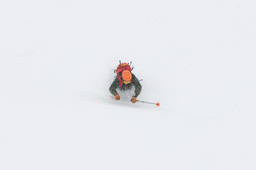 A skier with a backpack behind his back has lost his balance and flies into deep snow with his hands and ski poles outstretched