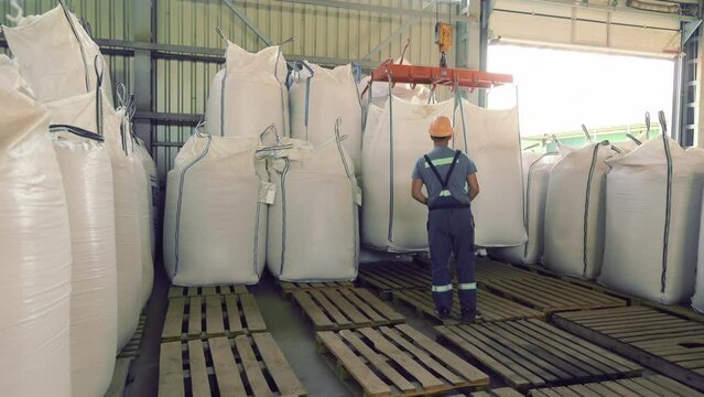 Worker Handling Large Bags in Warehouse, worker handling large bags in an industrial warehouse. The setting features heavy-duty equipment and pallets