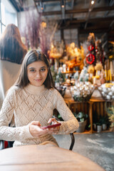 A beautiful, vibrant girl with a smartphone in hand at the Christmas decor store.