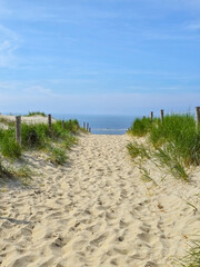 A serene path winds through lush green grass towards the sandy beach, inviting exploration and...