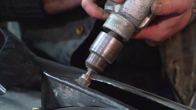 Hands of car worker grinding detail edges with carbide rotary burr rotation. Polishing holes in metal surface of car body using drill cone nozzle cutout. Close-up of working process, slow motion.