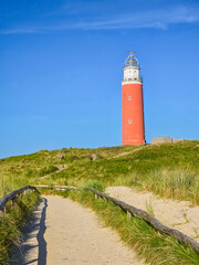 A vibrant red lighthouse stands proudly atop a lush green hill on the island of Texel, Netherlands.