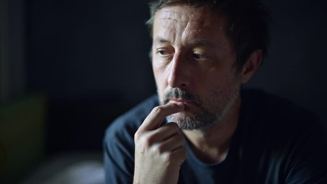 Contemplative mature adult man thinking in dark room and then looking out the window, depressed sulking male pondering