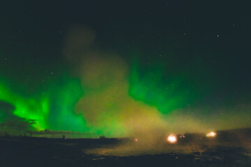 Beautiful aurora borealis over Geysir hot springs landmark in Iceland with eruptions. Travel...