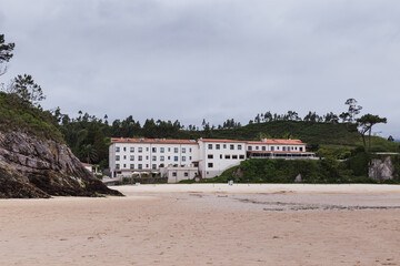 Rural hotel on a beach in northern Spain surrounded by green mountains with blackened trees and...