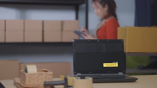A laptop shows a chat about order shipment status, with an Asian woman managing inventory in a small business. Cardboard boxes and packaging materials highlight e-commerce and logistics