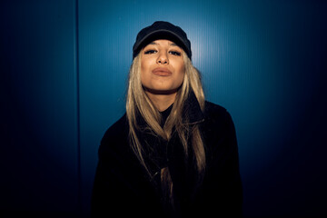 Caucasian attractive woman in black grunge attire posing against a blue wall