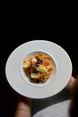 Person holding a plate of spaghetti with olives, cheese shavings, and anchovies, perfect for culinary blogs and restaurant promotions with copy space.