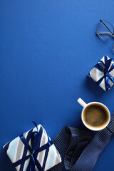 Stylish flat lay composition featuring striped gift boxes, glasses, coffee cup in a white mug, elegant tie on a vibrant blue background. Ideal for Fathers Day articles, promotional materials