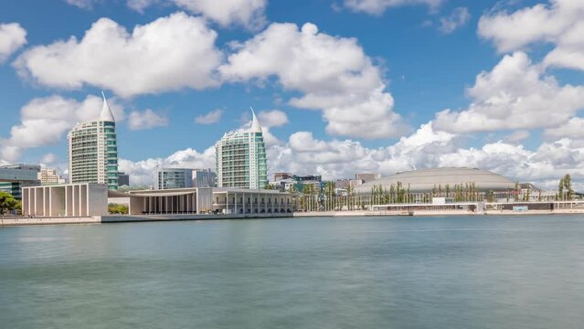 Panorama showing Parque das Nacoes or Park of Nations district timelapse in Lisbon, Portugal. Telecabine cable cars overlook Vasco da Gama bridge on Tagus river. Modern buildings reflected in water