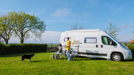 A man and his faithful dog stand next to an RV in a picturesque grassy field in Texel Netherlands,...