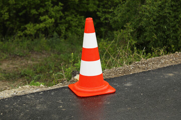 An orange construction cone indicates a portion of the road with a layer of fresh asphalt, traffic...
