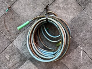 Dirty blue watering hose with sprinkler hanged on the wall outside a house