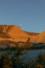 the moon is rising in the distance as it sets over a rocky cliff