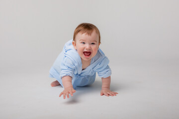 A cute happy laughing baby in a soft bathrobe crawls on a white background after bathing. The child is wrapped in a clean and dry towel. Washing, baby hygiene, health and skin care