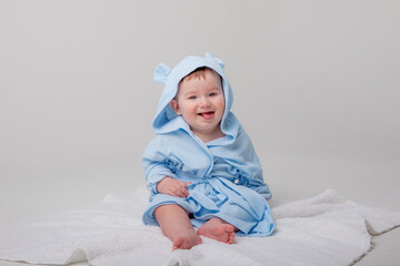 Cute happy laughing baby in a soft bathrobe after bathing plays on a white background. The child is wrapped in a clean and dry towel. Washing, baby hygiene, health and skin care
