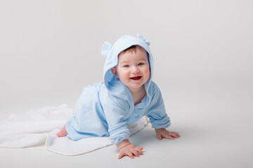 A cute happy laughing baby in a soft bathrobe crawls on a white background after bathing. The child is wrapped in a clean and dry towel. Washing, baby hygiene, health and skin care