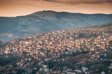 panorama of Sarajevo as the sun sets behind its rolling hills, casting a colorful hue over the...