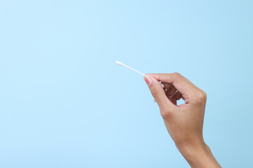 Woman's hand holding a cotton bud isolated on blue background