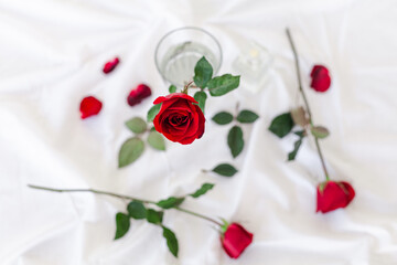 a red rose on top of a bed next to a glass and two spoons