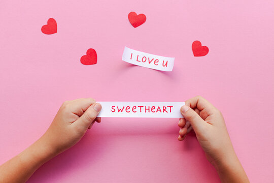 two hands holding paper hearts and writing i love you on pink background
