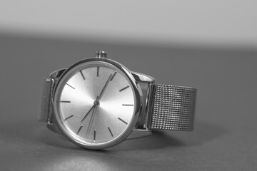 A silver watch with a black face sits on a gray surface