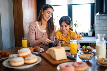Cheerful supportive mother having breakfast with her adorable preschool age daughter.