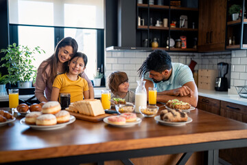 Happy father and mother having breakfast with two small children at dinning table in the kitchen at home.