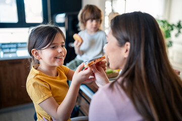 Small young daughter enjoying to share, feeding her mother. Daughter having breakfast with her mom.